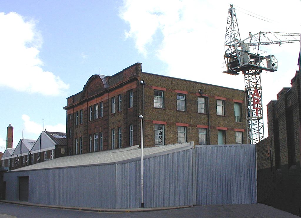Old brick building with arched windows and a construction crane behind under a clear sky. | Valerieg, Public domain, via Wikimedia Commons