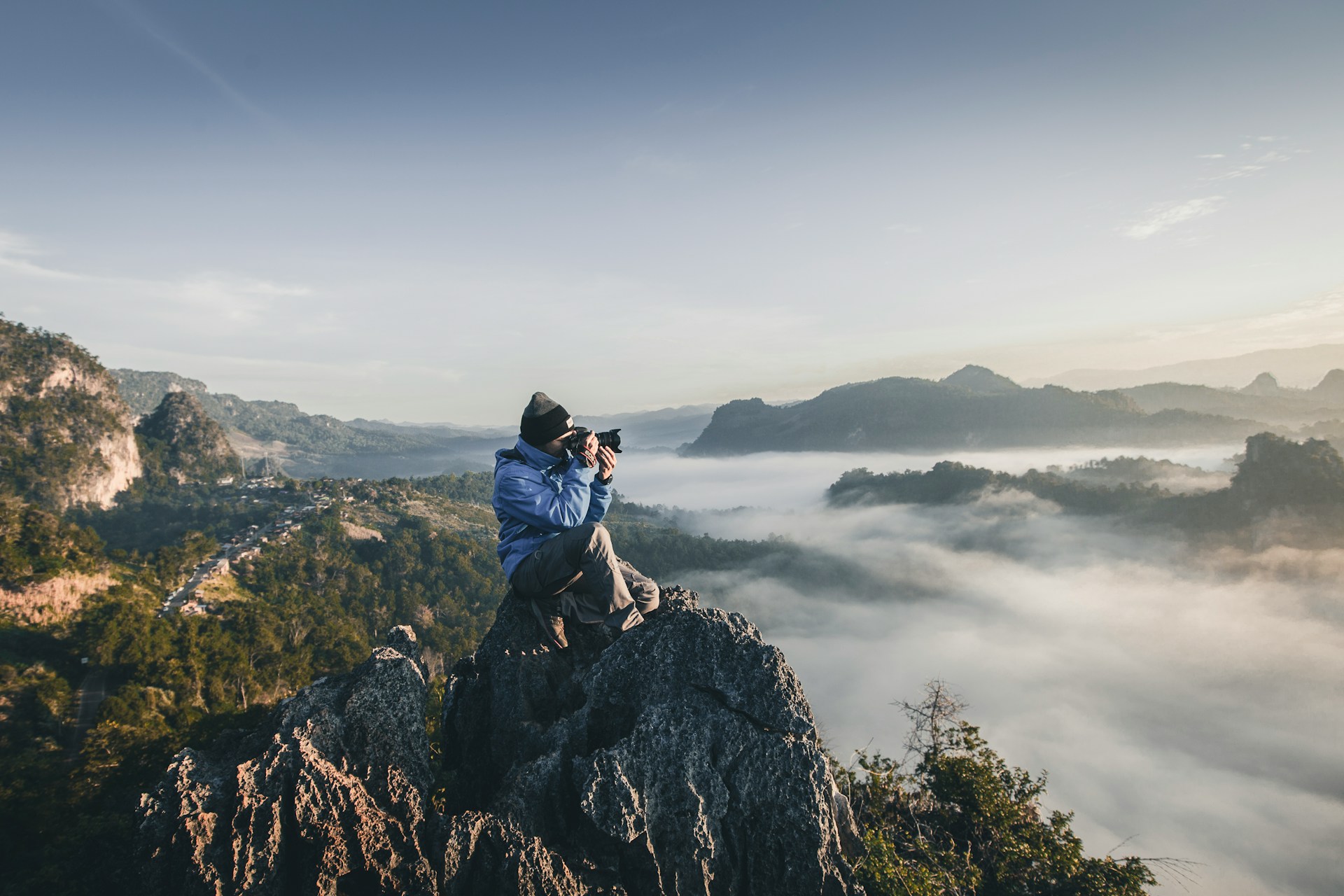 Photographer sitting on a mountain peak over a misty valley at sunrise. | Photo by Alif Ngoylung on Unsplash