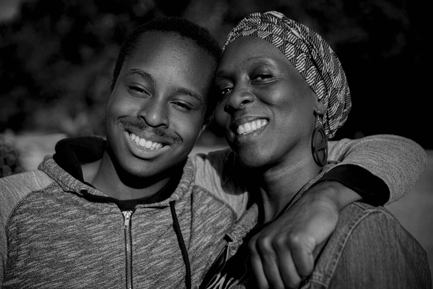 Two black peole in casual wear sitting closely together, one with a patterned headscarf, in monochrome. | Wayne Campbell 2024
