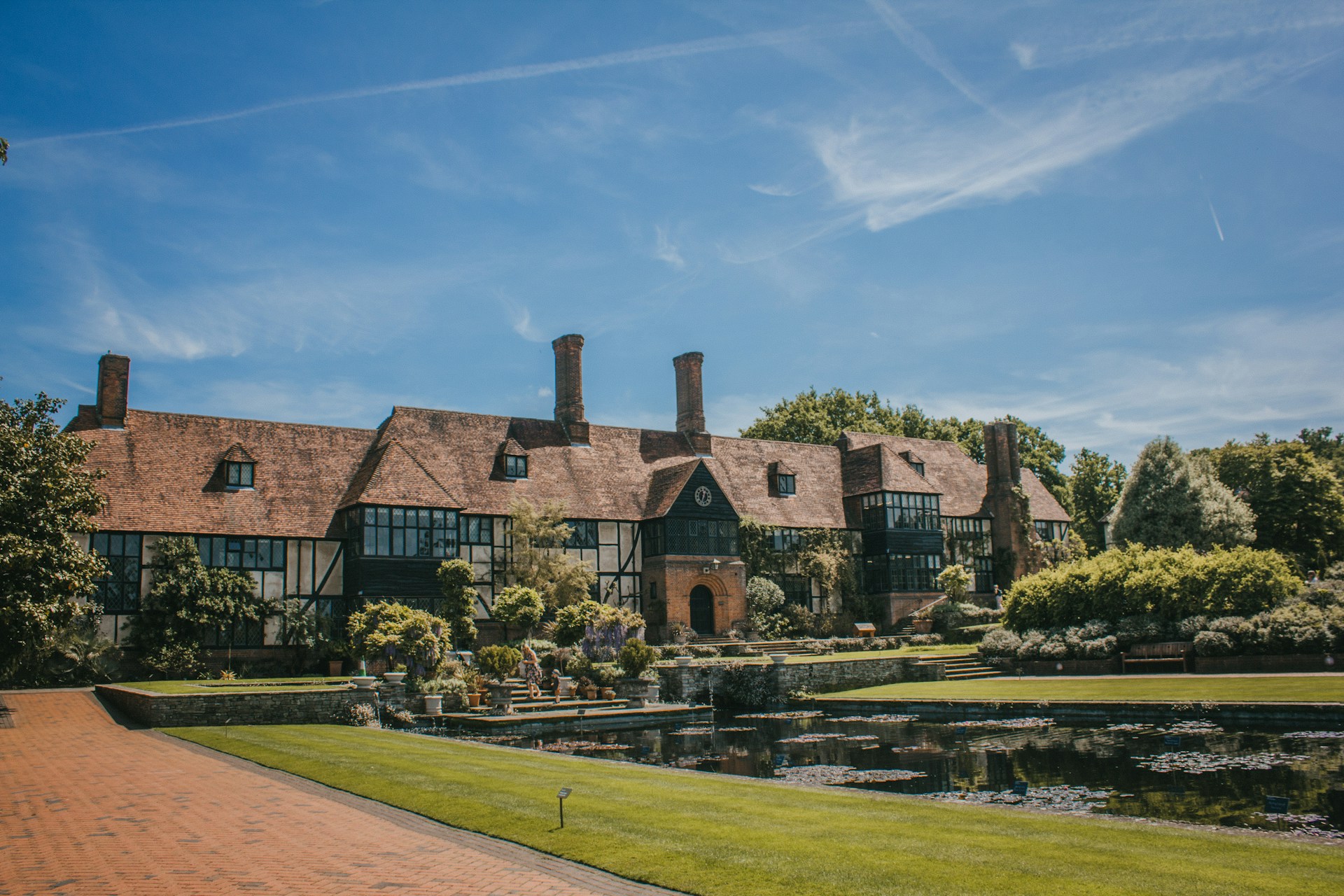 Traditional Tudor-style house with garden and pond under a clear blue sky. | Photo by Jemima Whyles on Unsplash