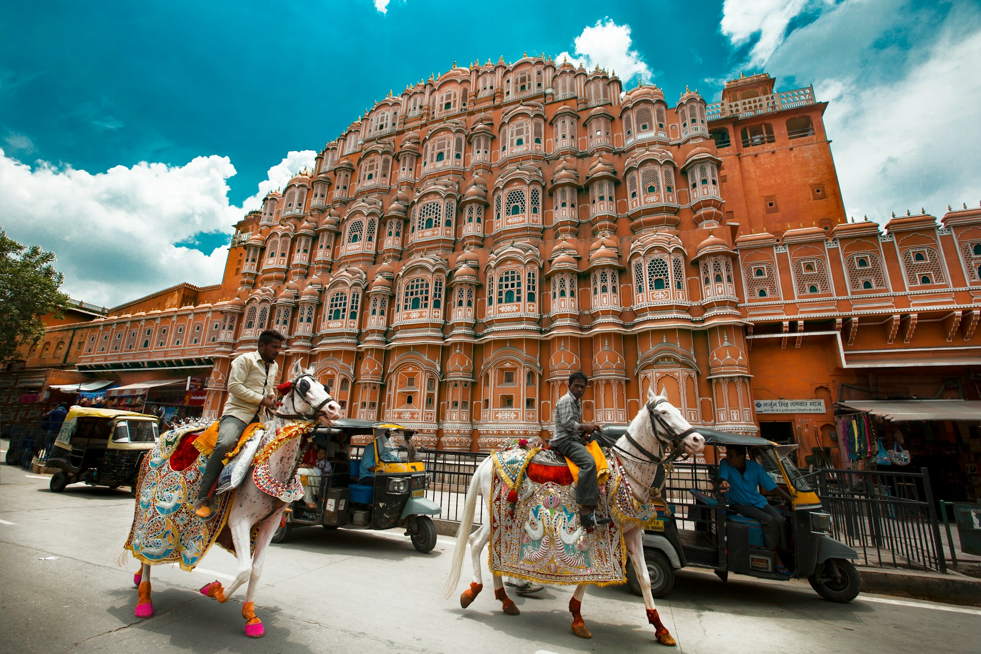 Decorated horses in front of Hawa Mahal, under a cloudy sky. | Photo by Aditya Siva on Unsplash