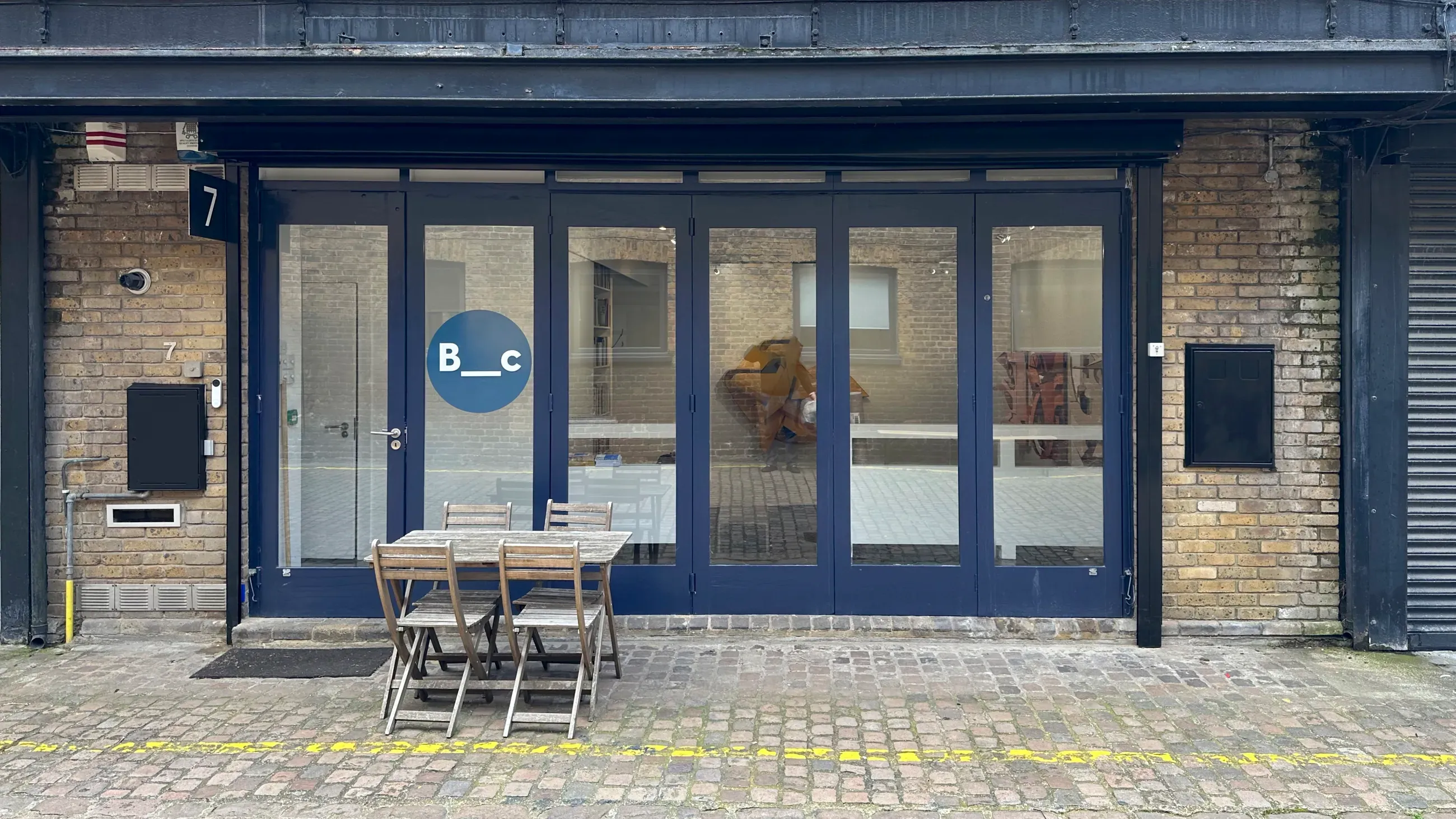 Storefront with a blue facade, number 7, and a wooden table set outside. | Bartha Contemporary