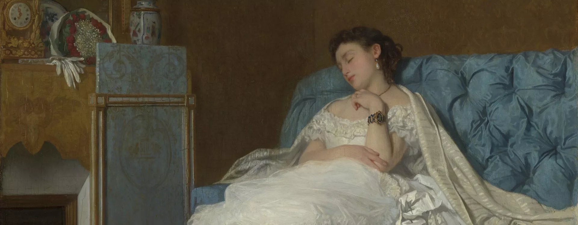 Woman in white dress reclining on a blue sofa, with a painting and flowers in the background.