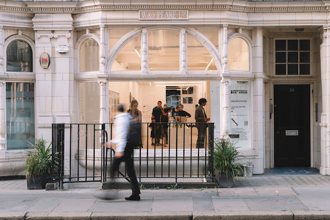 Elegant storefront with pedestrians, one blurred in motion, and a group inside conversing. | Ab-Anbar Gallery