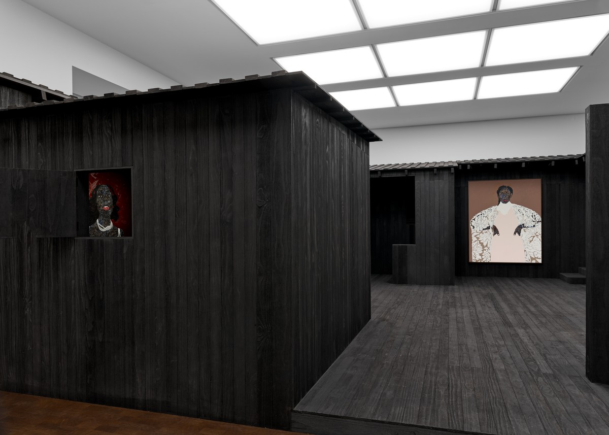 A gallery featuring dark wooden structures with artworks of figures on the walls, illuminated by daylight from a ceiling panel.