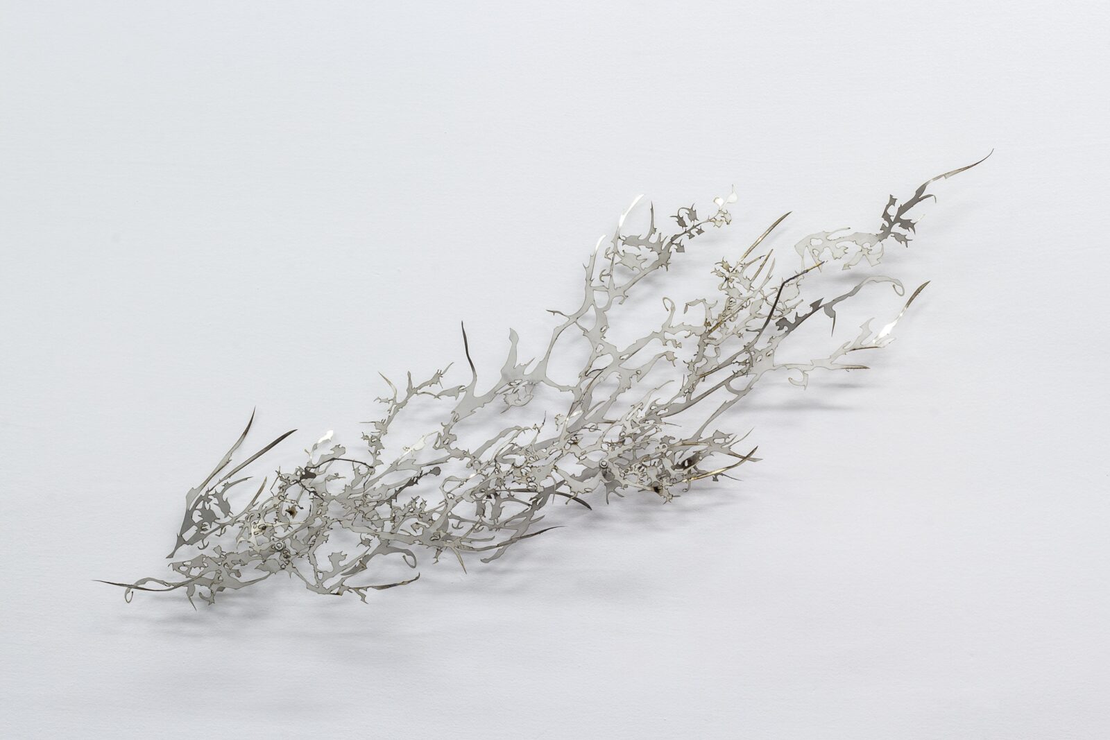 A delicate, intricately designed metallic sculpture resembling organic branches, set against a clean white background.