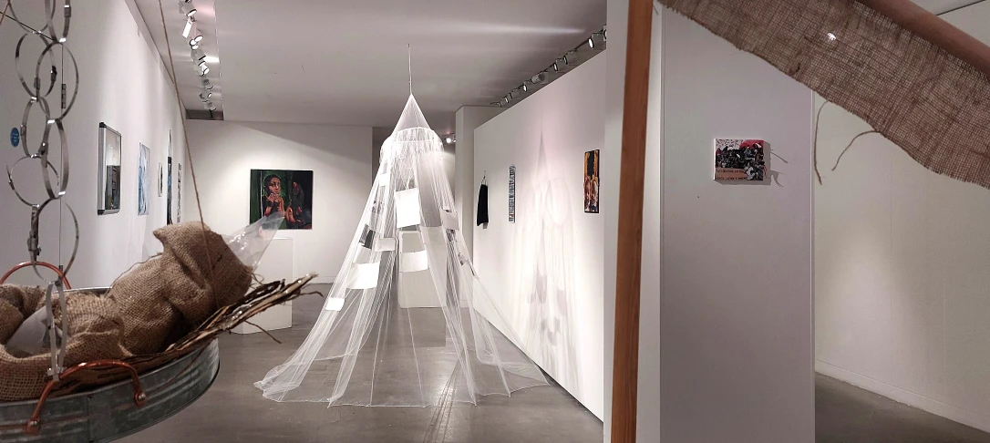 Art gallery interior featuring a translucent sculpture, framed artwork on the walls, and a woven basket with burlap, creating an inviting atmosphere.