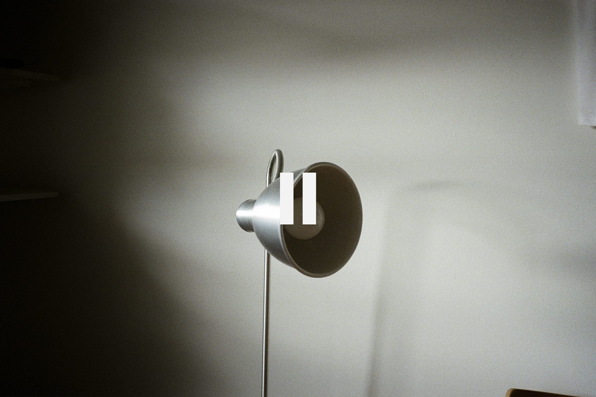 A modern silver lamp emits soft light against a neutral wall, casting gentle shadows in a cozy, minimalist space. | 2025 New Art Projects