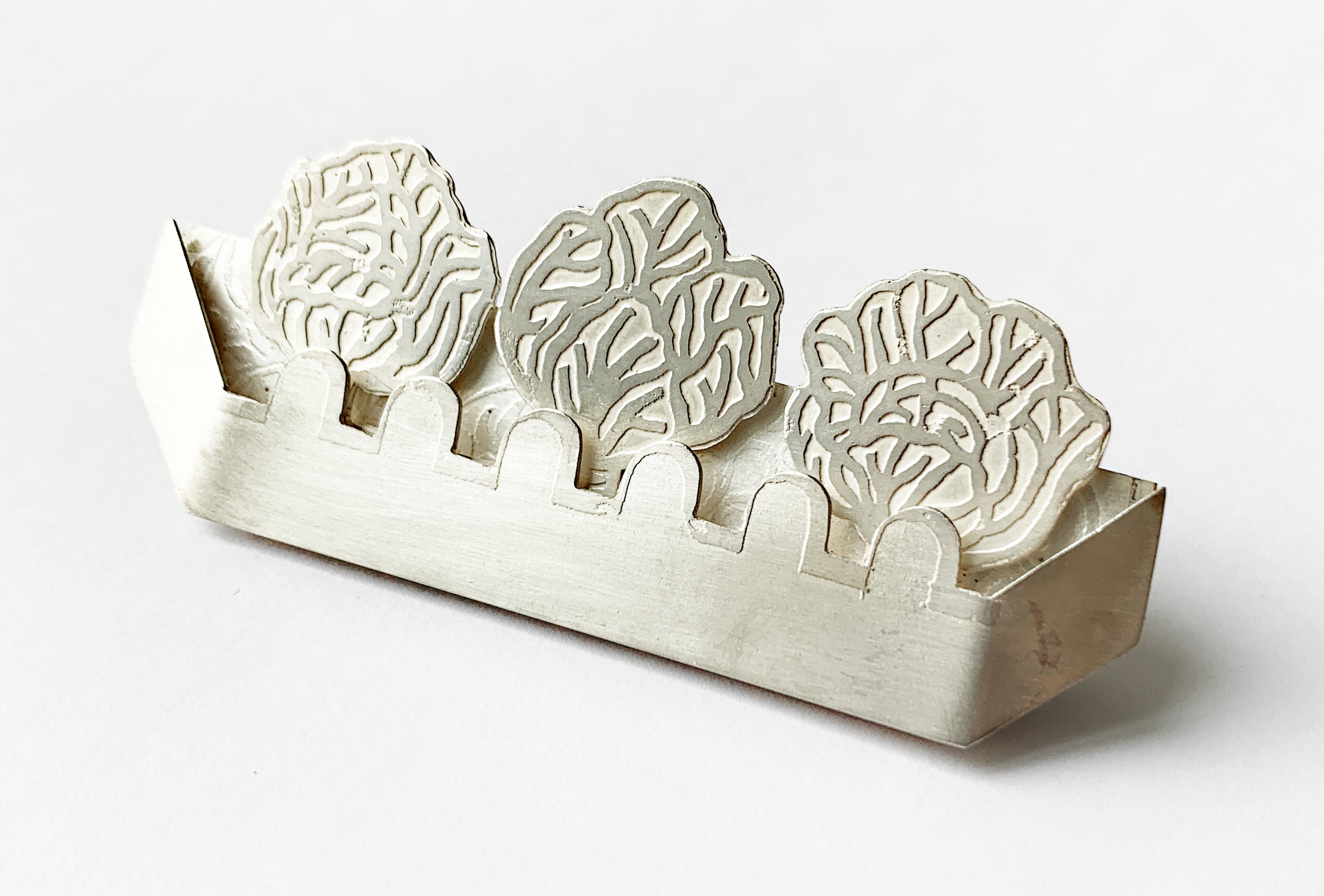 A silver decorative holder featuring three intricately designed floral shapes, resting on a scalloped base.
