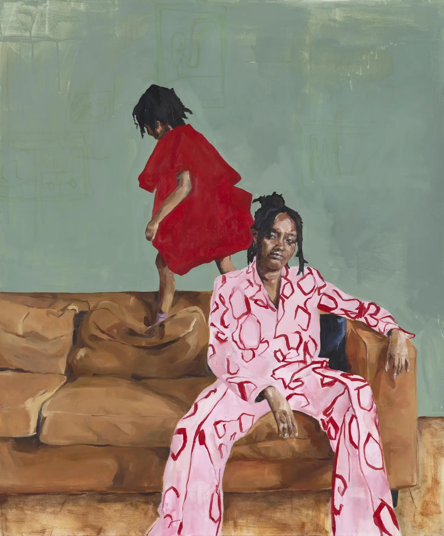 A woman in a pink patterned outfit sits on a brown couch, while a girl in a red dress playfully stands on the cushions.