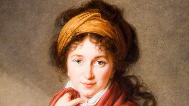 A person with curly hair draped in an orange headscarf, wearing a richly colored garment, stands against a neutral background.