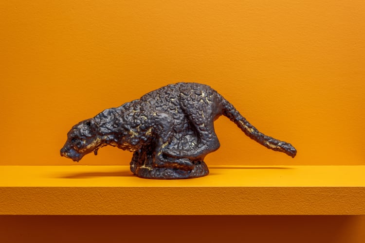 A statue of a cat sitting on a yellow shelf indoors.