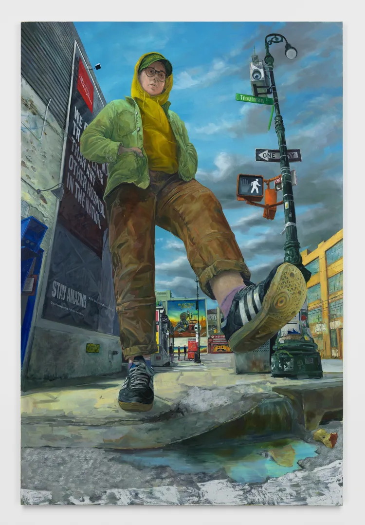 A person wearing a green jacket and yellow hoodie stands on the edge of a sidewalk, with urban street signs and a lively backdrop.