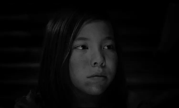 A girl with long hair, looking thoughtfully off to the side, against a dark background.