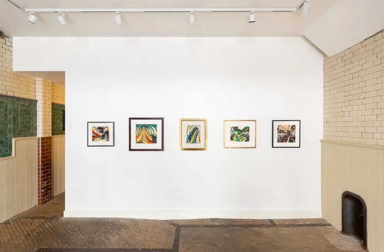 A gallery wall featuring five framed artworks displayed in a minimalist setting.