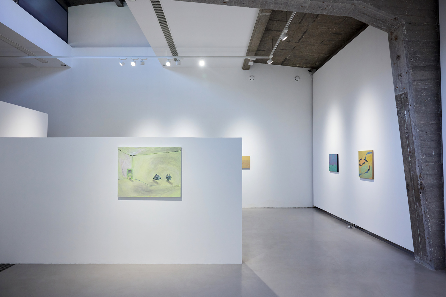 Minimalist contemporary art gallery with white walls, concrete floors, exposed beams, and colorful paintings under bright track lighting.